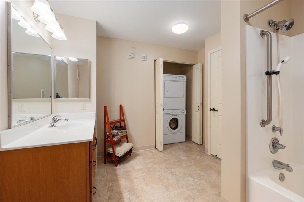 A bathroom with a sink, mirror, and a washer and dryer.