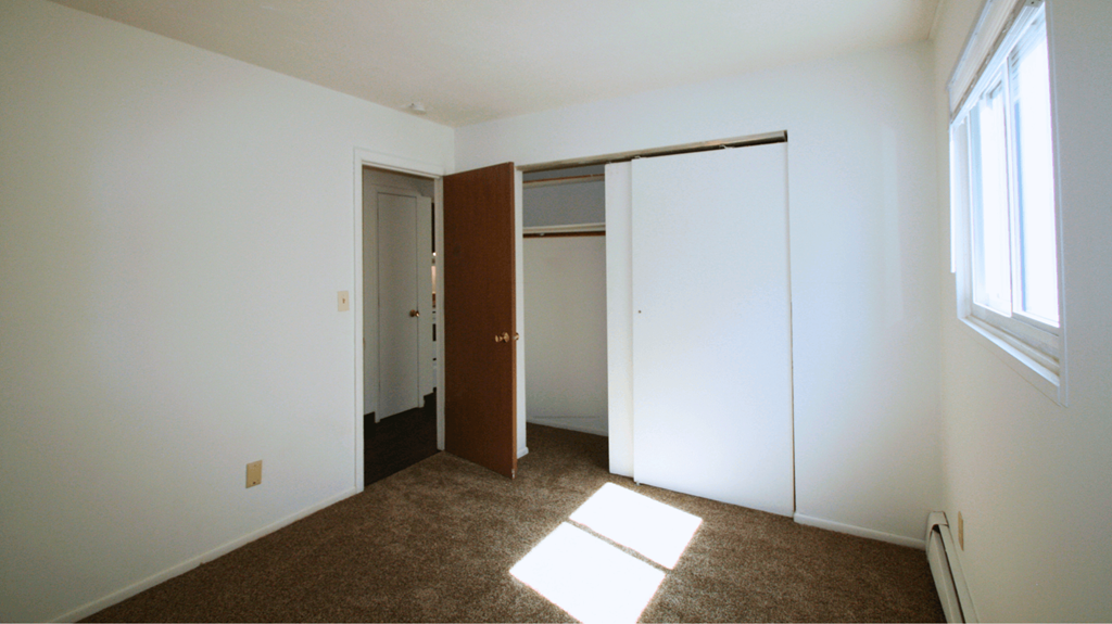a bedroom with white walls and a door to a closet