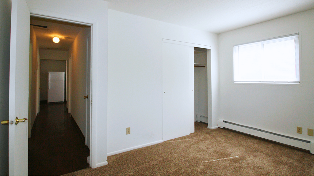 a bedroom with a carpeted floor and a door to a hallway and a closet