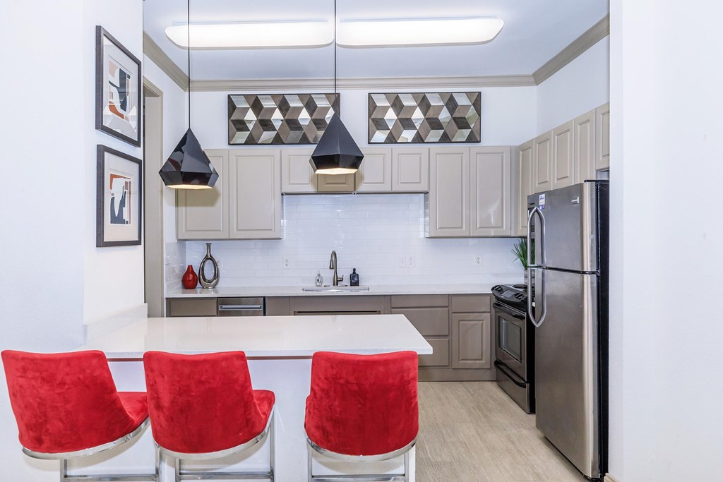 A modern kitchen with a white island and red chairs.