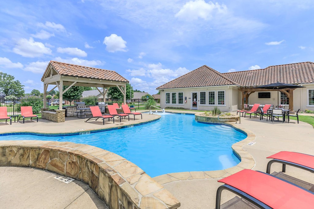 A large outdoor swimming pool with red lounge chairs and a gazebo.