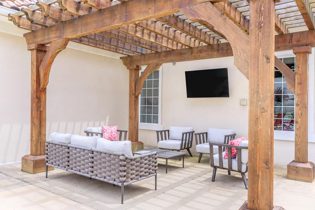 A wooden pergola with a grey sofa and chairs underneath.