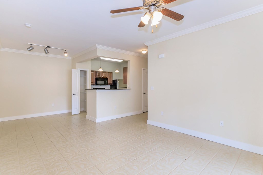 A spacious living room with a ceiling fan and a kitchen area in the background.
