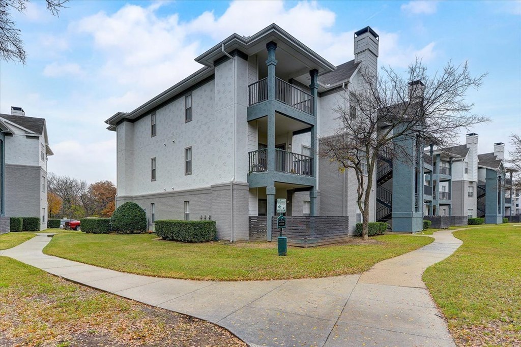 a white apartment building with a sidewalk and grass