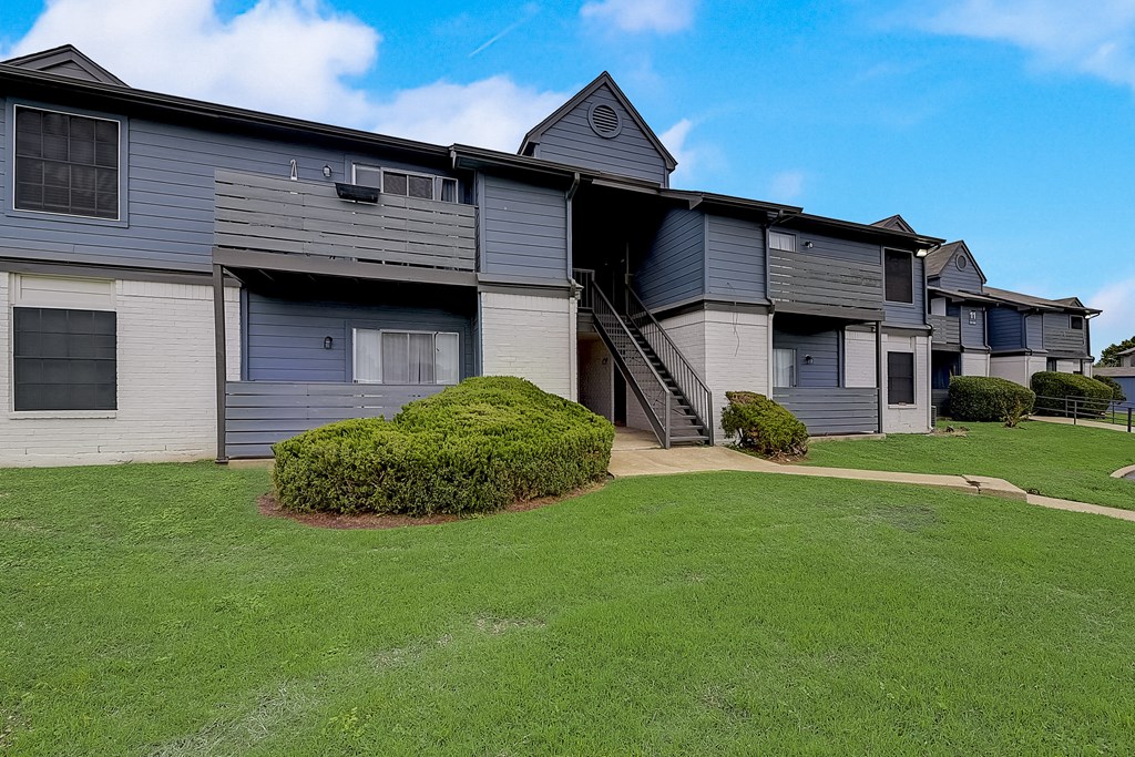 a large gray and white apartment building with a green lawn