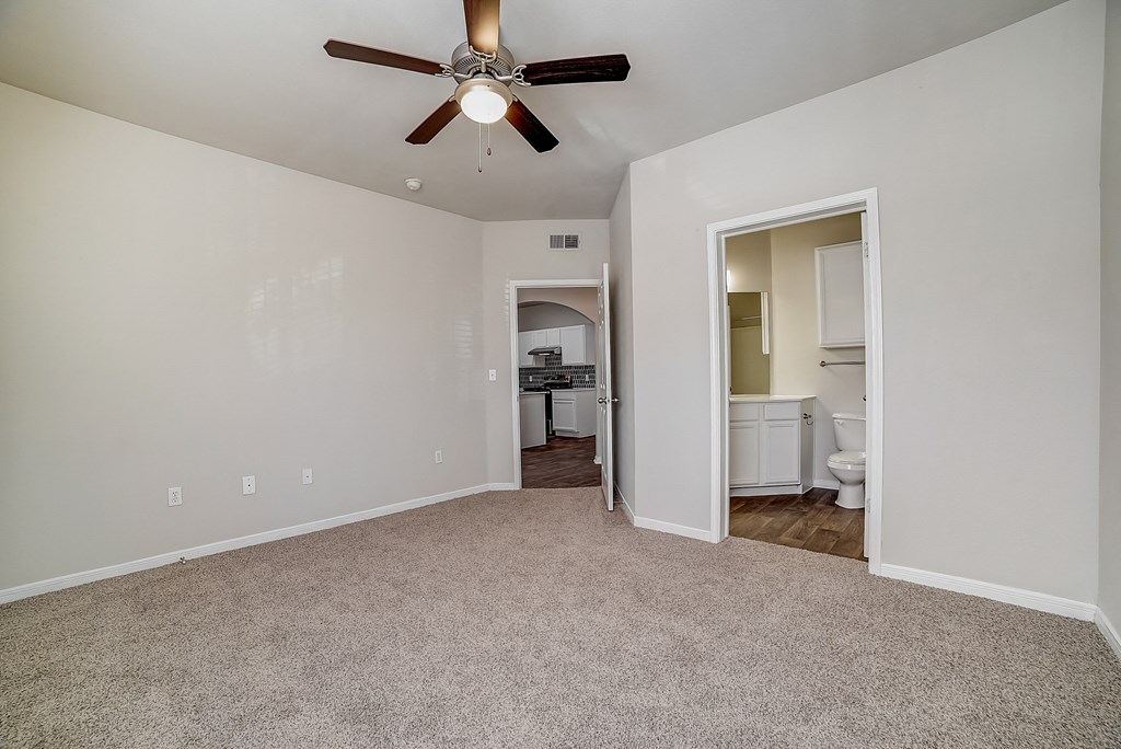 an empty living room with a ceiling fan and a door to a kitchen