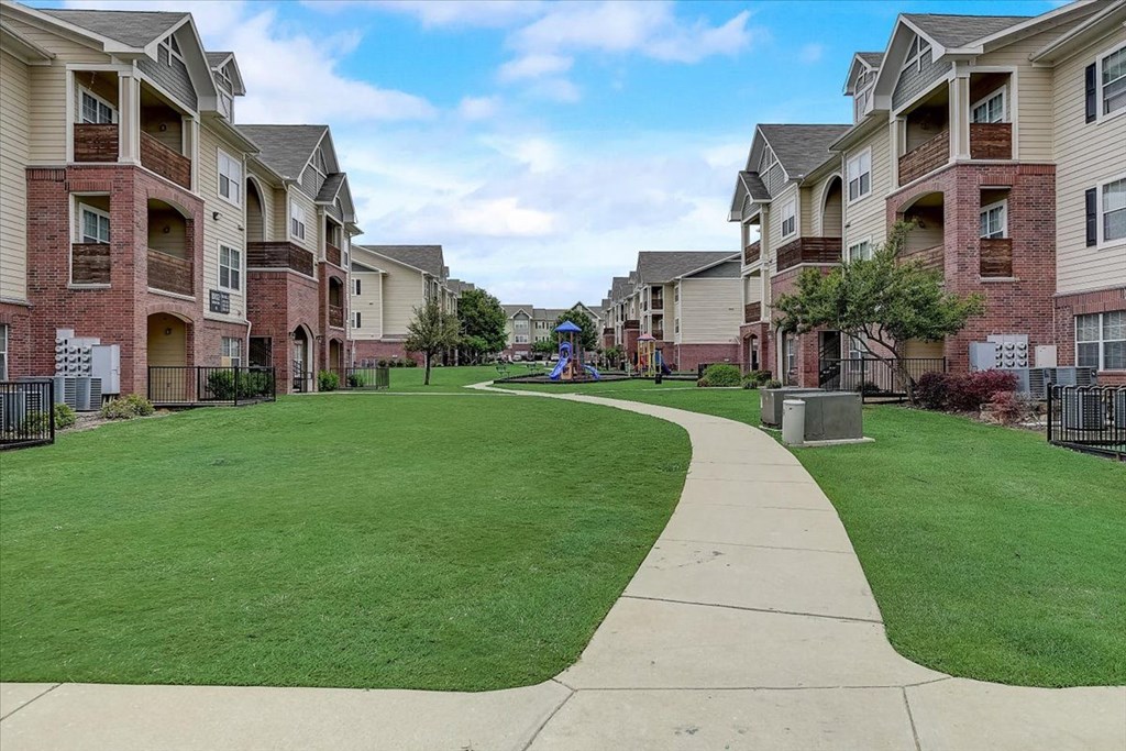a grassy area with a playground in front of an apartment complex