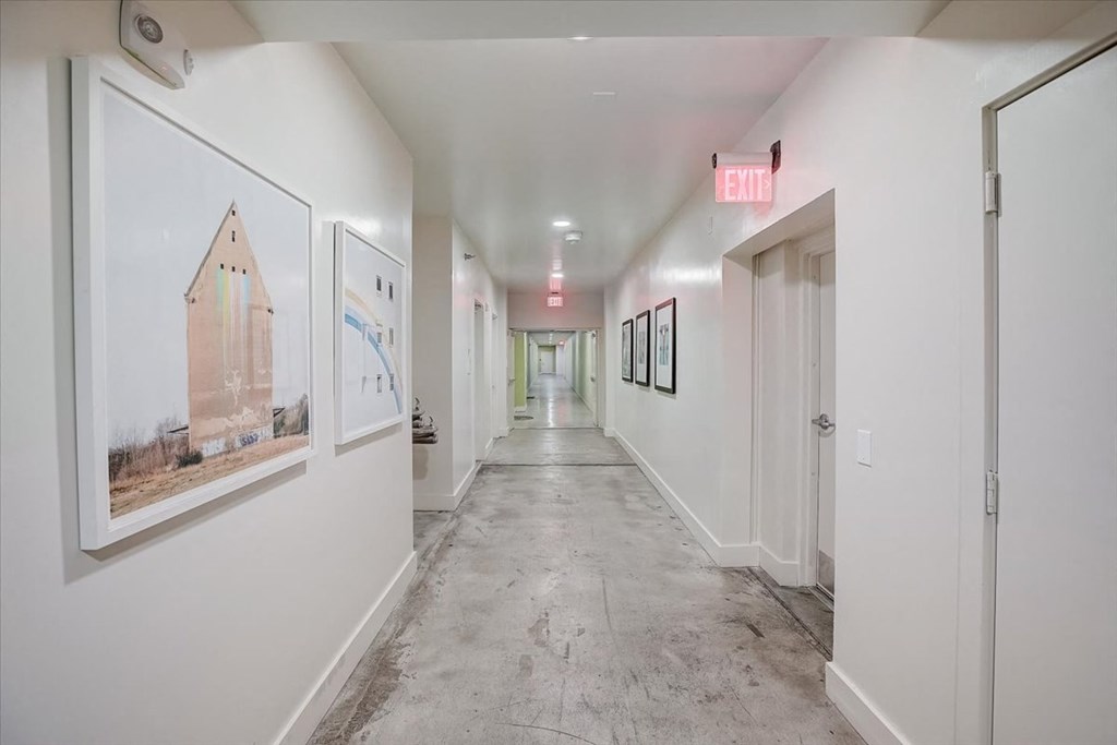 a long white hallway with paintings on the wall and a exit sign