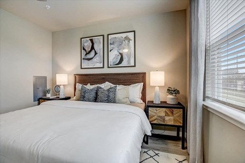 Inviting bedroom with wood headboard, bedside lamps, and a sunlit window with blinds.