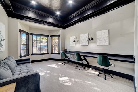 Coworking room with built-in counter, rolling chairs, and sofa seating under dark ceiling.