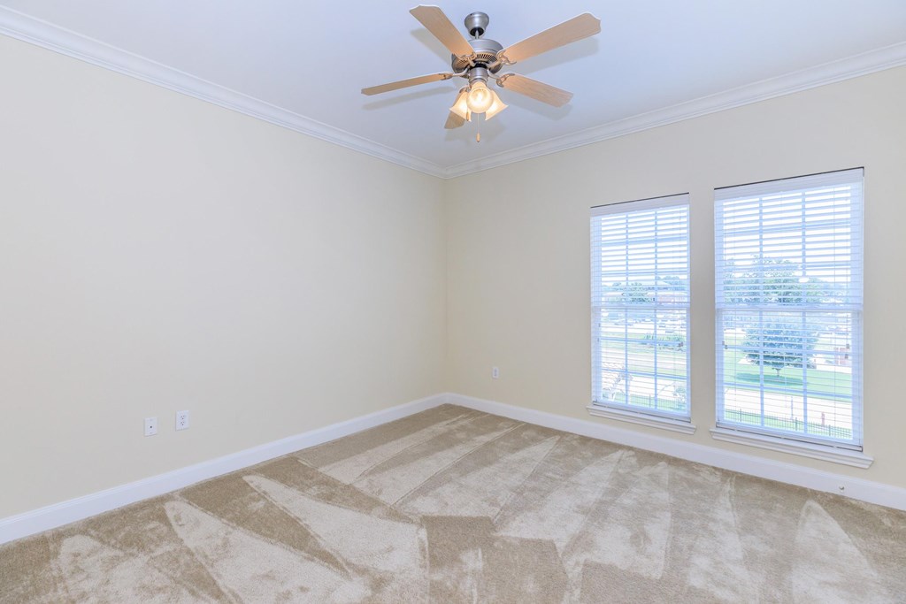A room with a ceiling fan and two windows.