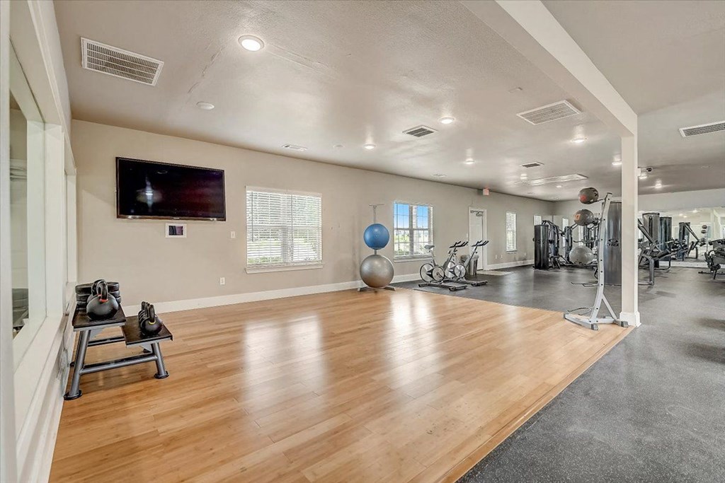a large fitness room with hardwood floors and a flat screen tv on the wall