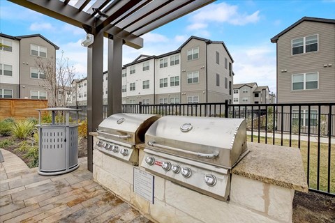Outdoor grilling area with stainless gas grills, stone counters, and covered pergola for cookouts.
