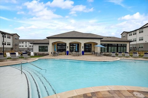 Swimming pool with wide steps, sun deck loungers, and clubhouse backdrop in Hutto, TX.