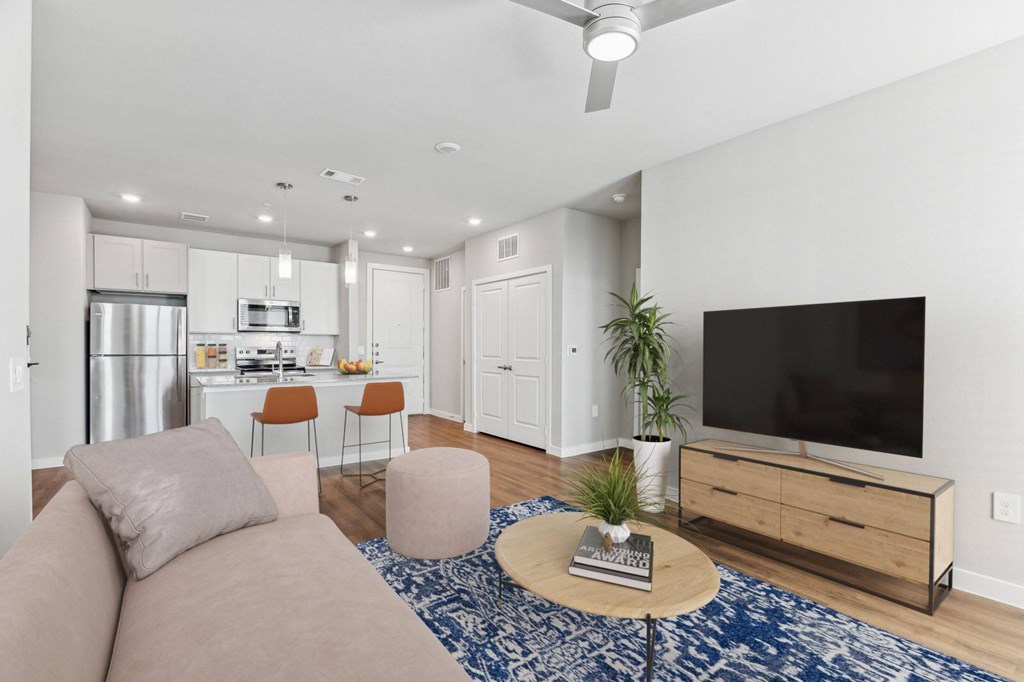 A modern living room with a flat screen TV, a kitchen area, and a dining area.