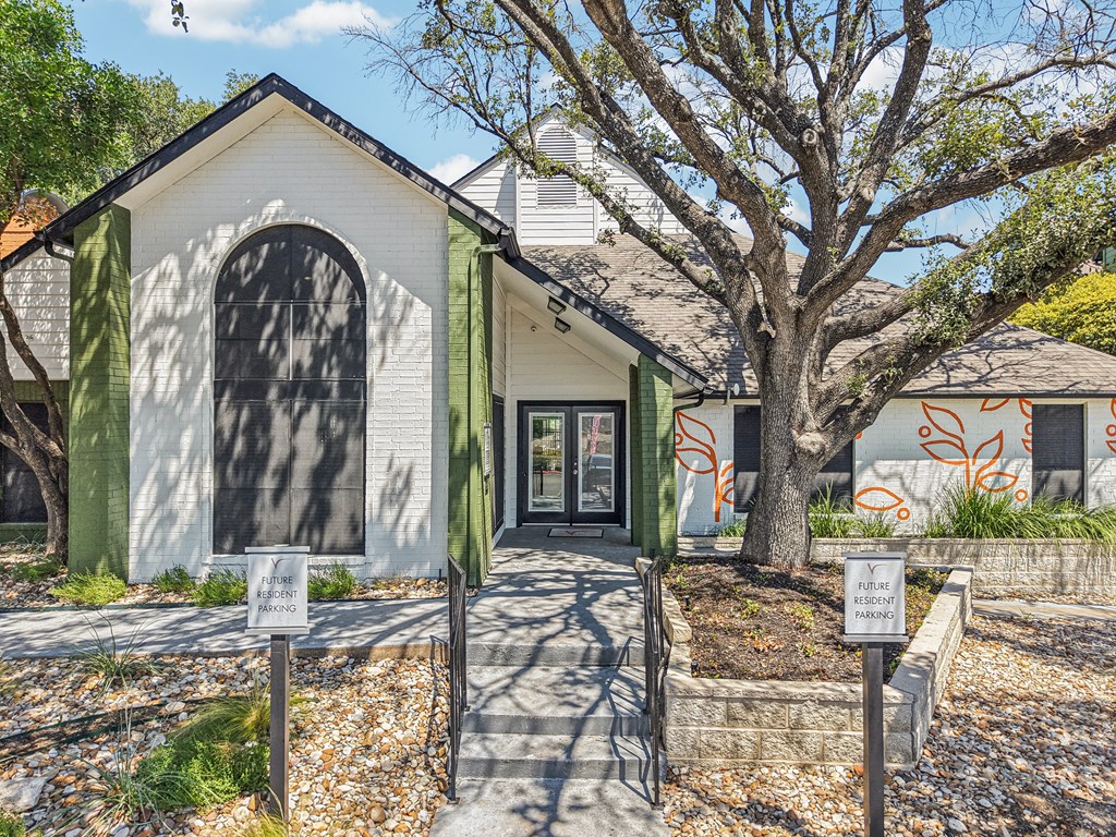 A white building with a green trim and a tree in front.