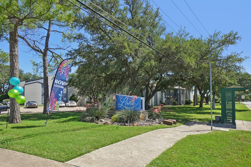 A blue sign with white writing is on a fence in front of a building.