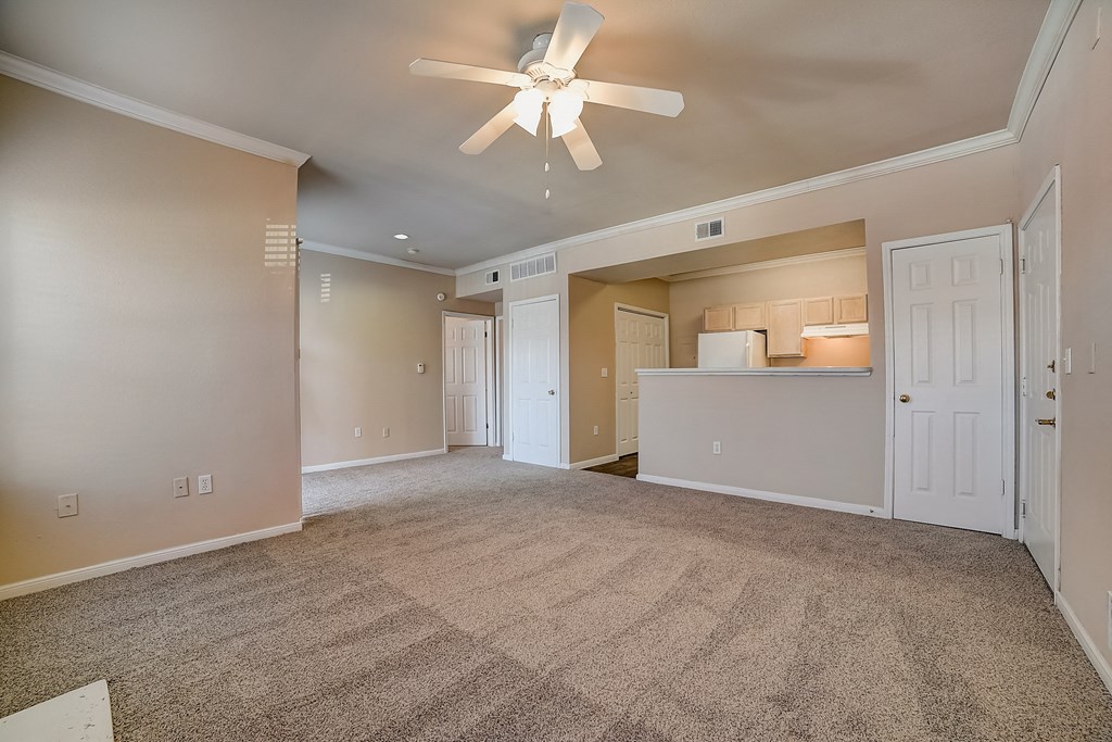 an empty living room with a ceiling fan and a kitchen
