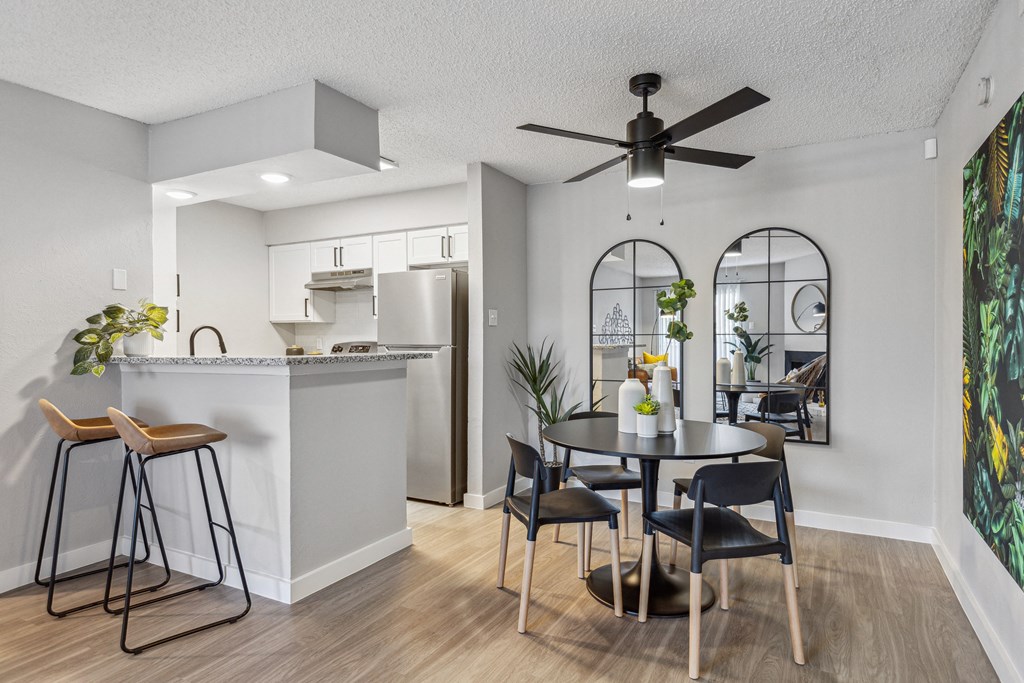 a dining area with a table and chairs and a kitchen in the background