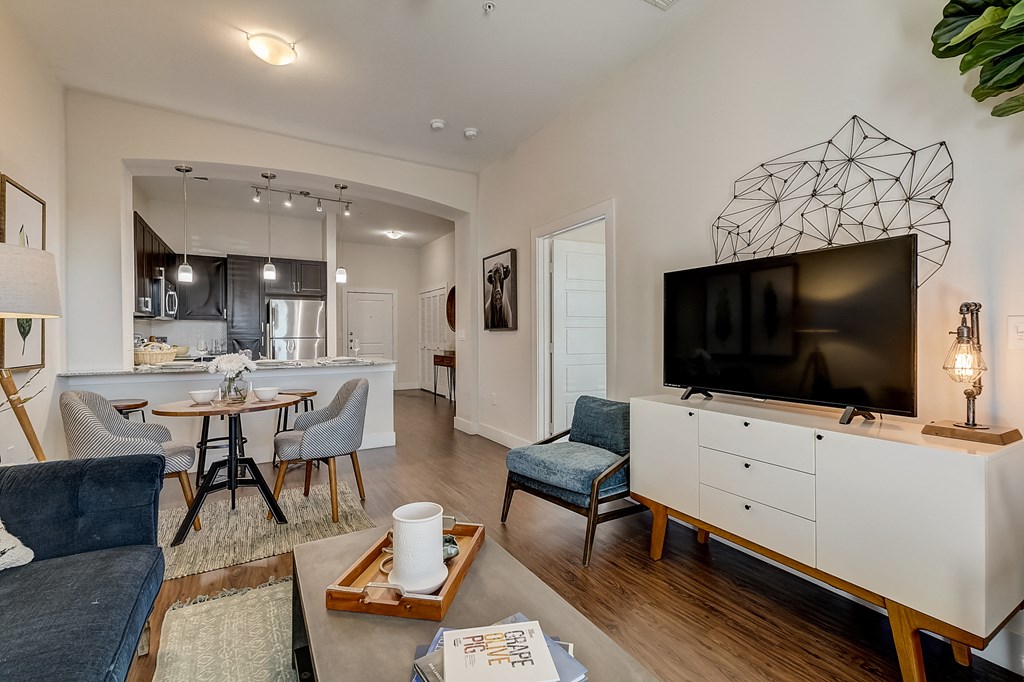 a living room with a large tv and a kitchen with a table and chairs