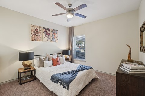 A bedroom with a bed, a ceiling fan, and a painting on the wall.
