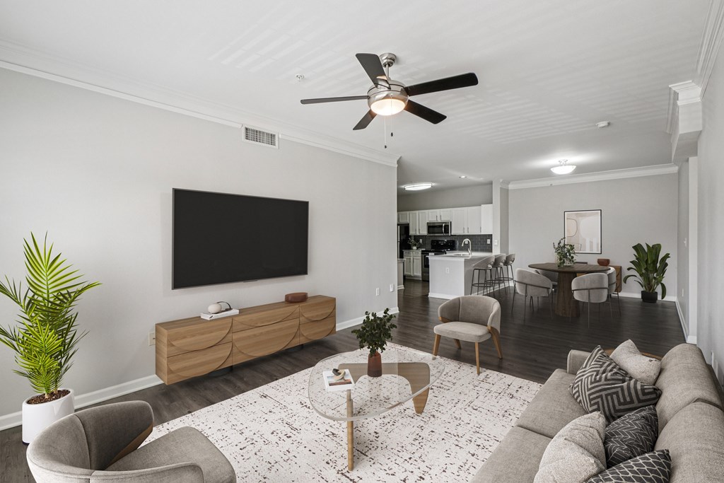A living room with a grey couch, a coffee table, a flat screen TV, and a ceiling fan.