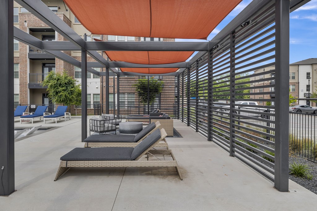 a covered patio with lounge chairs and tables and a metal fence