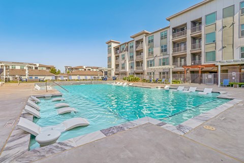 A large swimming pool with lounge chairs is surrounded by apartment buildings.