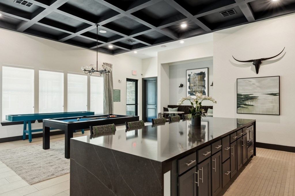 A modern kitchen with a pool table and a large painting of a bull's head.