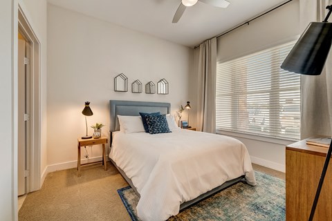 A bedroom with a bed, a nightstand, and a window with blinds.