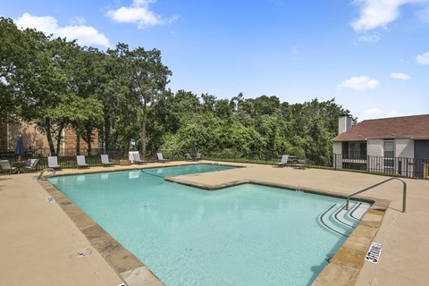 A large outdoor swimming pool surrounded by trees and lounge chairs.