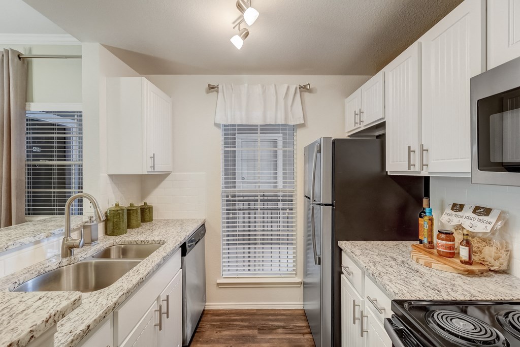 a kitchen with white cabinets and granite counter tops and a stainless steel refrigerator