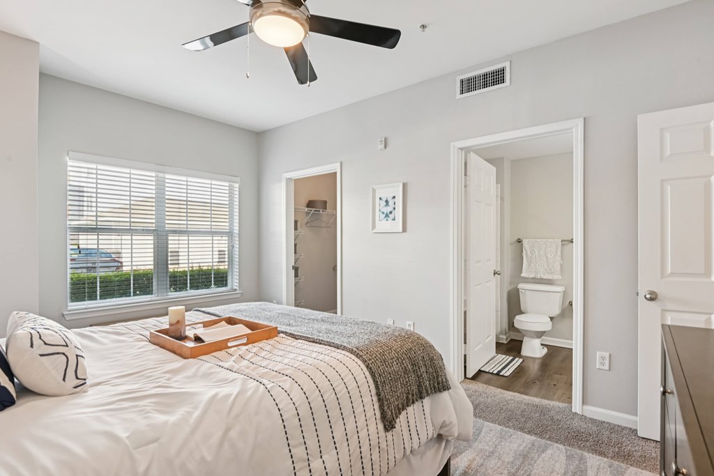 A bedroom with a bed, a ceiling fan, and a bathroom visible through an open door.