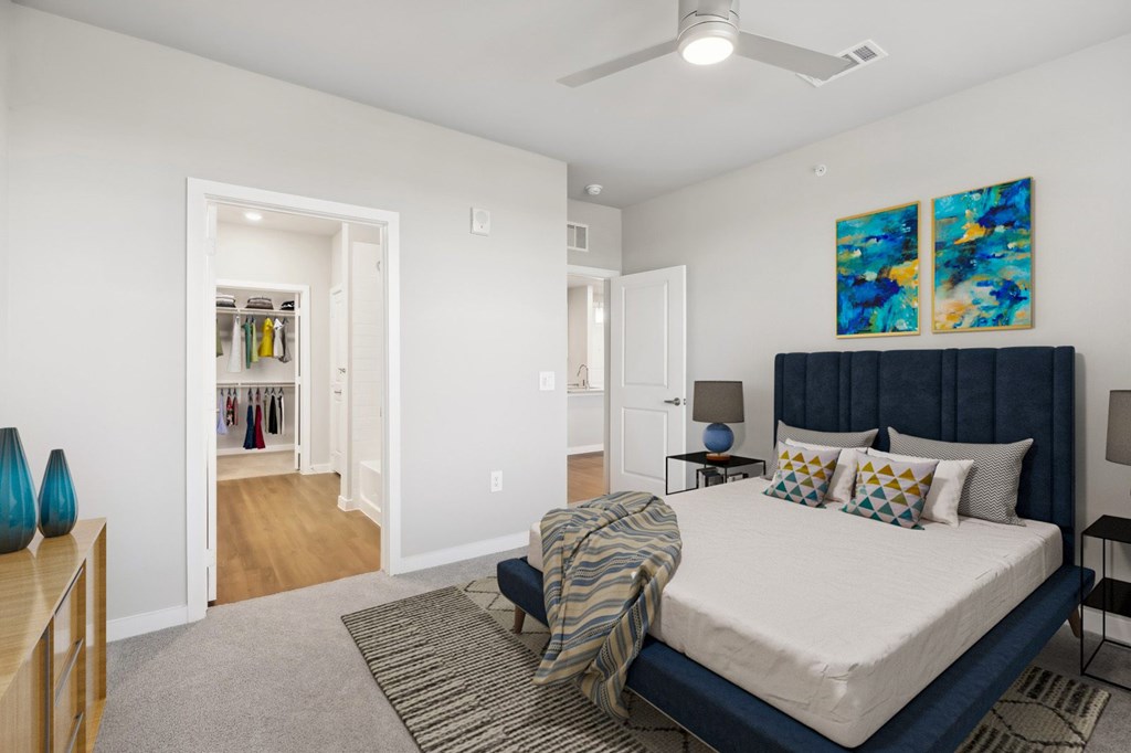 A bedroom with a bed, a ceiling fan, and a painting on the wall.