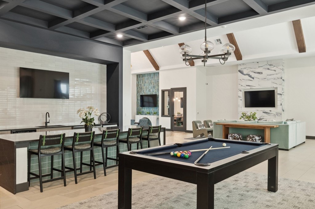 A pool table is in the middle of a room with a bar and a television.