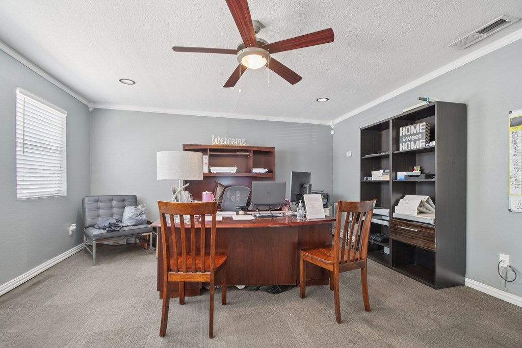 A room with a desk, chairs, and a ceiling fan.