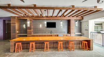 A bar with orange stools and a wooden counter is set up under a wooden beam.