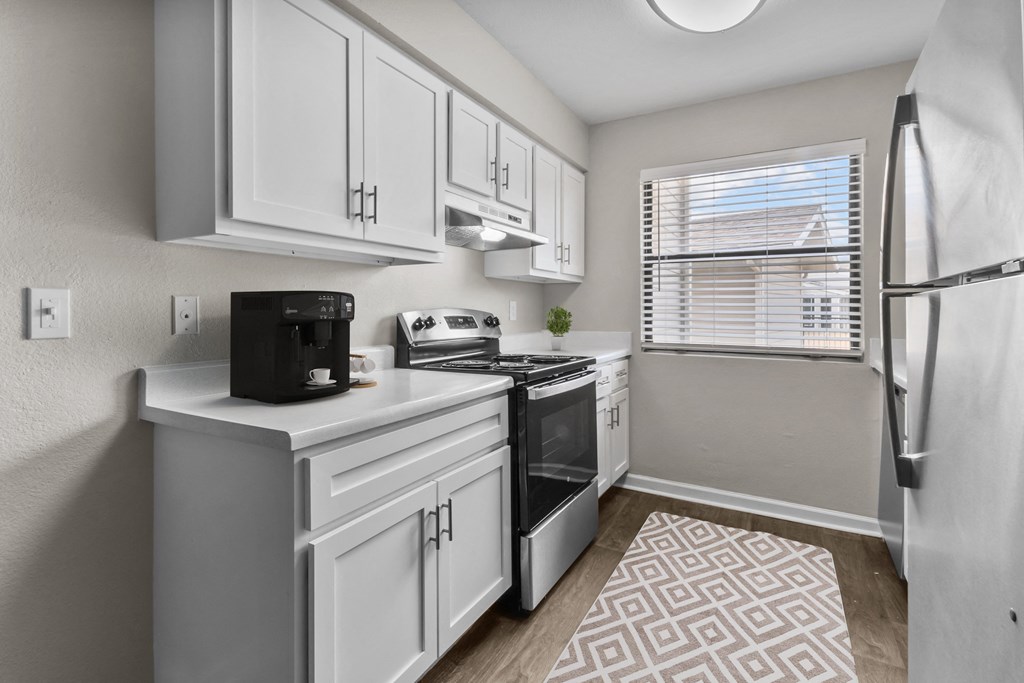 an open kitchen with white cabinets and a window and a refrigerator