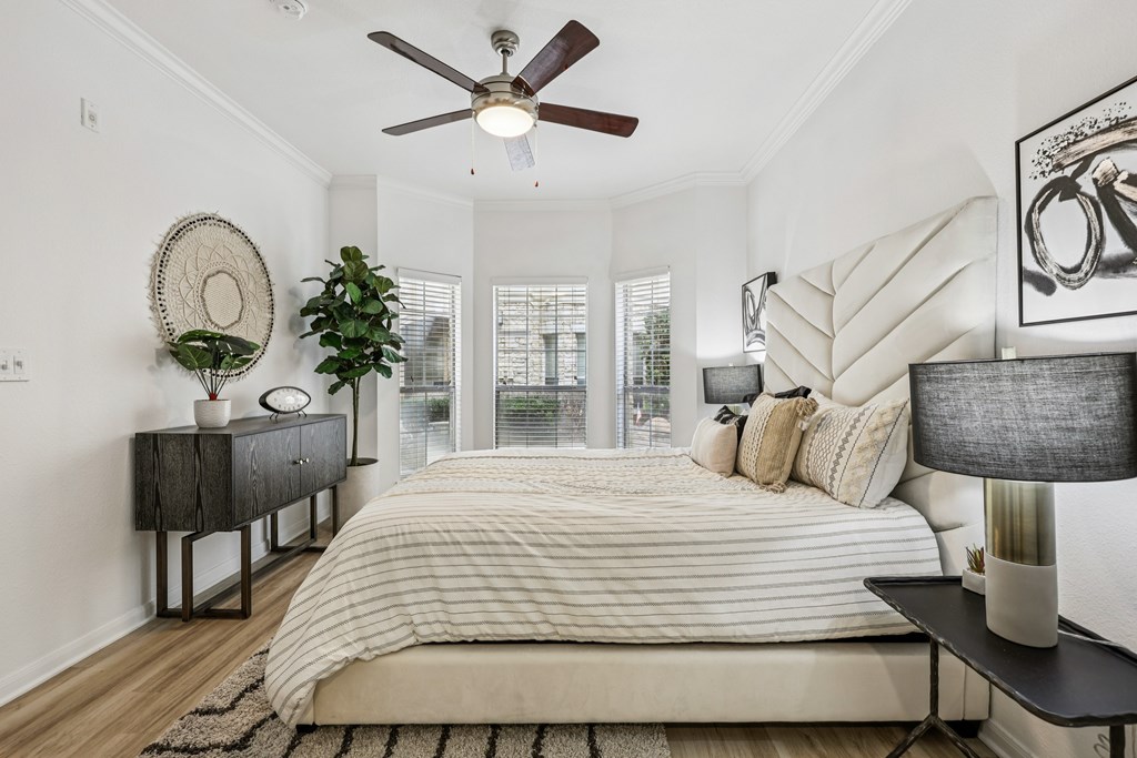 A bedroom with a large bed, a ceiling fan, and a side table with a plant.