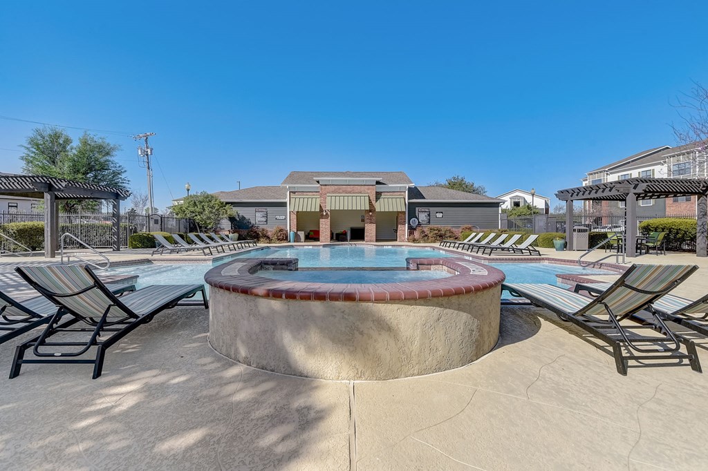 a pool with chairs and a hot tub with a building in the background