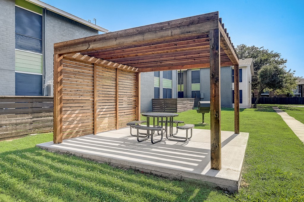 a wooden pergola with a table and chairs on a concrete patio