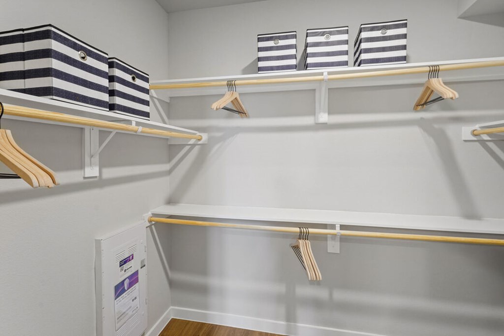 A white closet with clothes hanging and bins on the shelf.