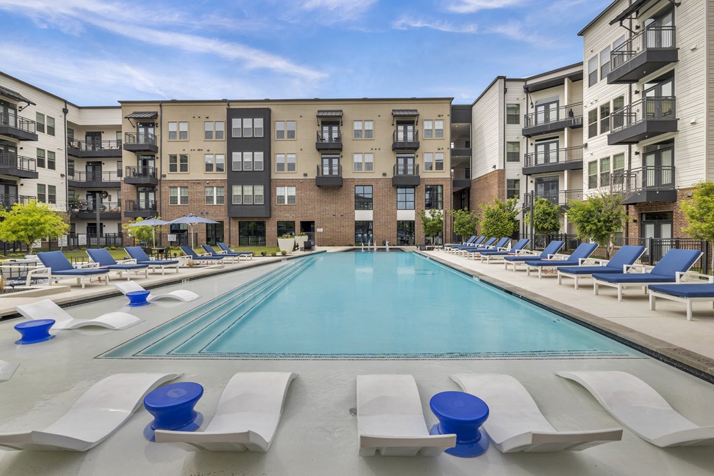 a swimming pool with lounge chairs in front of an apartment building