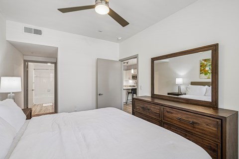 A bedroom with a large bed, a ceiling fan, and a mirror with a wooden frame.