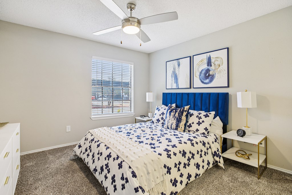 A bedroom with a bed, a ceiling fan, and a window with blinds.