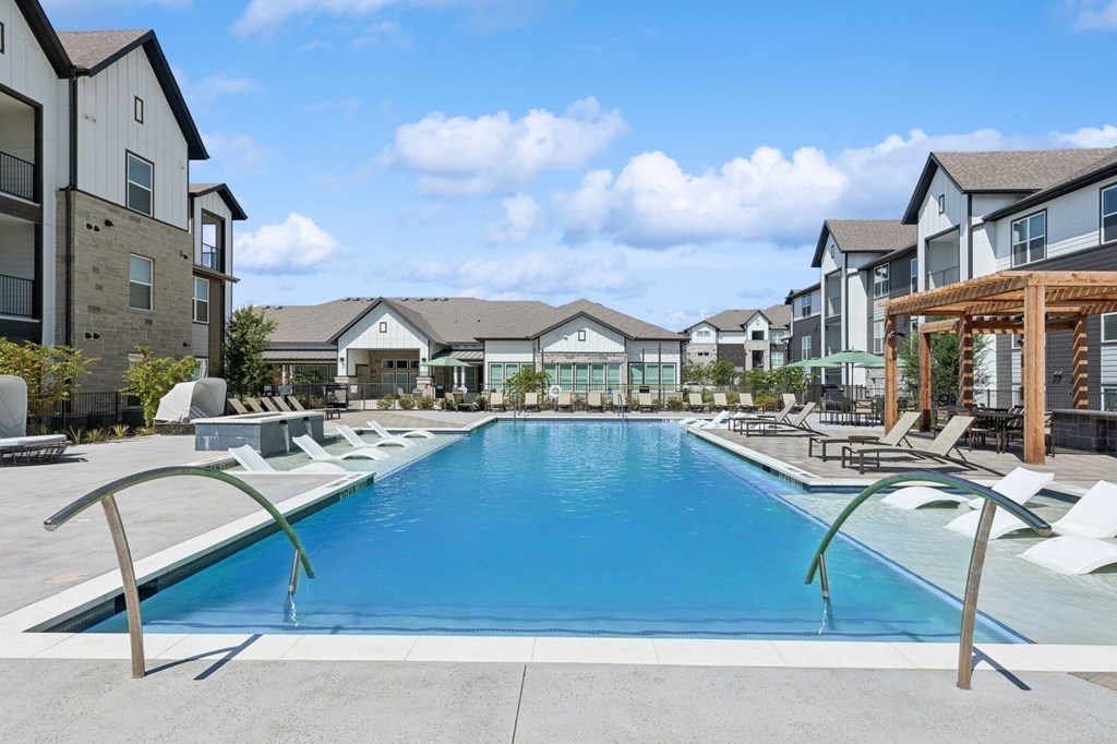 A large swimming pool surrounded by lounge chairs and buildings in the background.