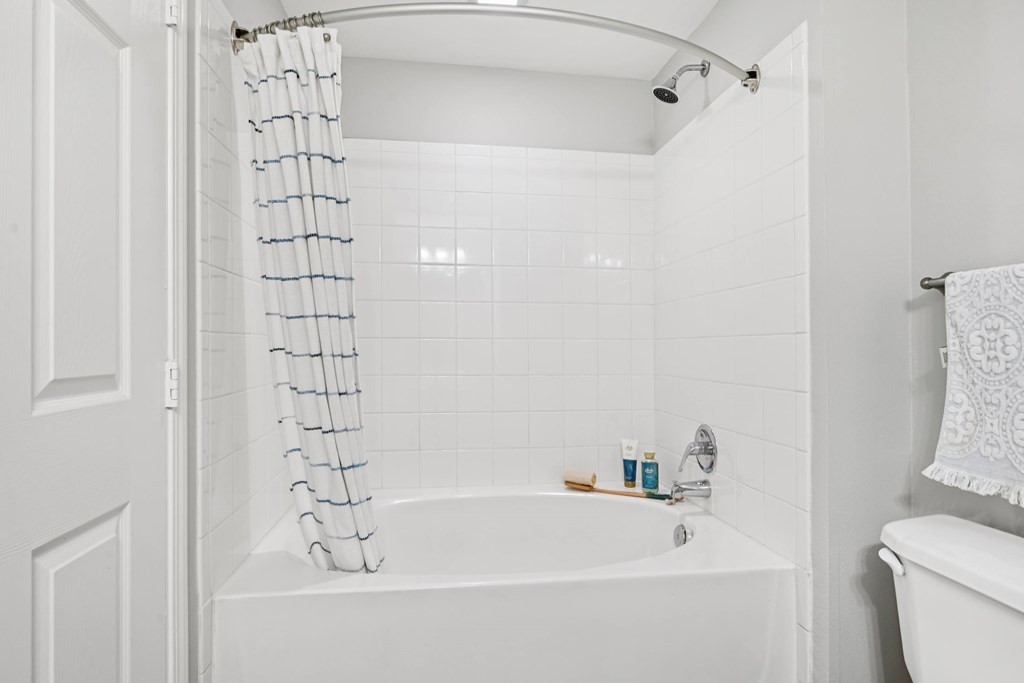 A white bathroom with a white tub and a white shower curtain.