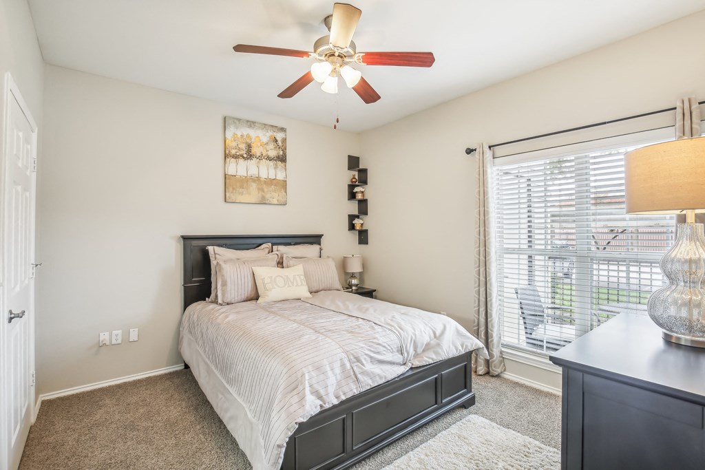 A bedroom with a bed, a ceiling fan, and a painting on the wall.