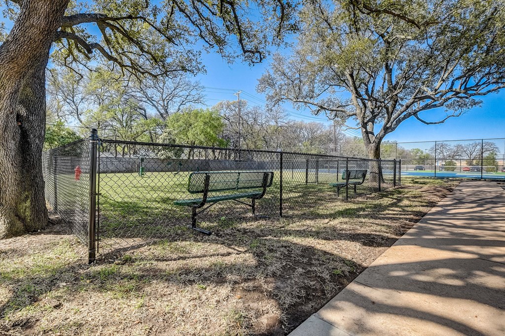 two park benches in front of a fence near a tennis court