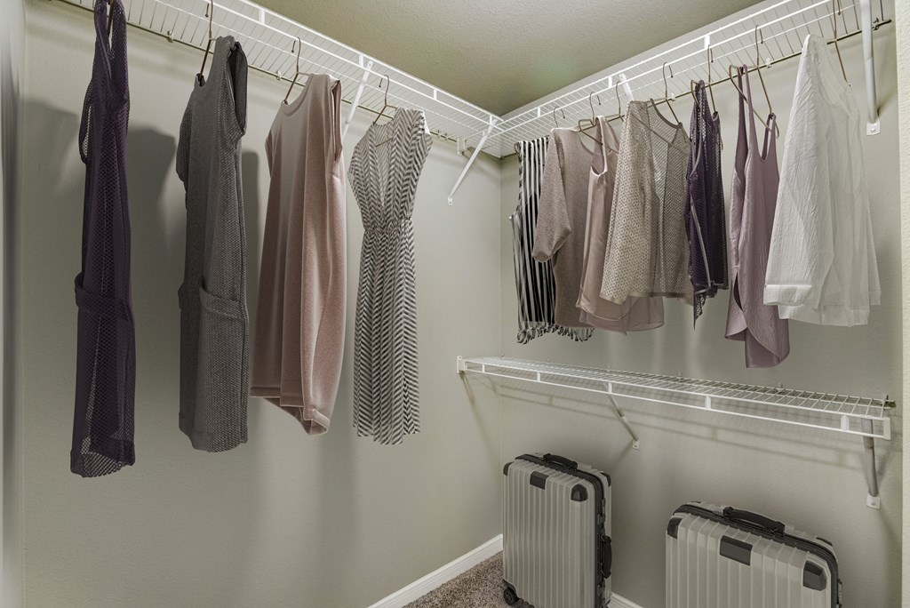 a closet with clothes hanging on a rack and luggage on the floor